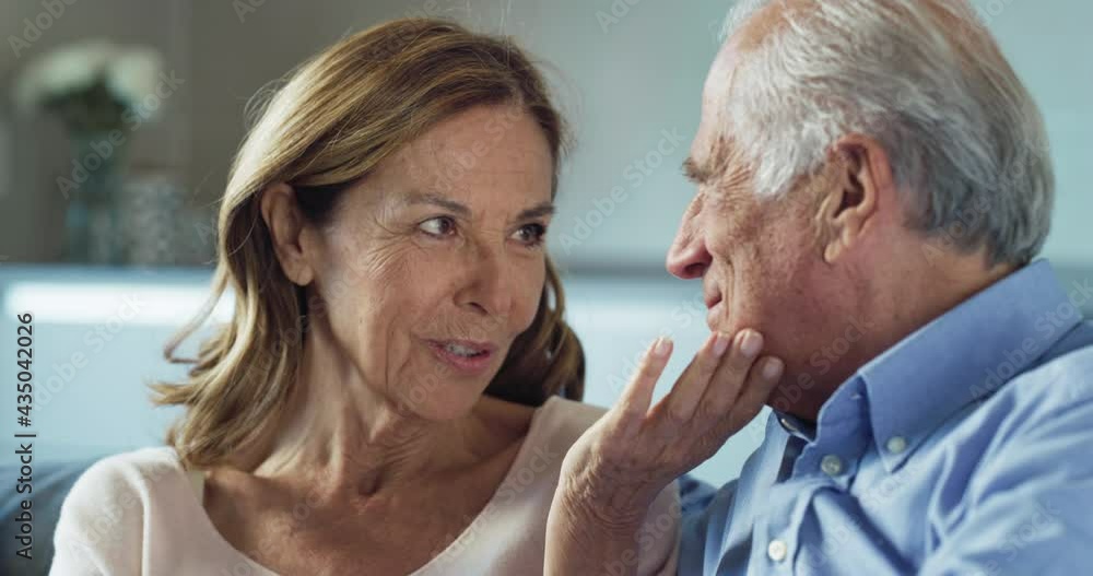 Cinematic shot of lovely happy mature couple enjoying time together is speaking and caressing each other with affection while sitting on sofa at home. Concept: love, family, marriage, happiness, age Cinematic shot of lovely happy mature couple enjoying time together is speaking and caressing each other with affection while sitting on sofa at home. Concept: love, family, marriage, happiness, age