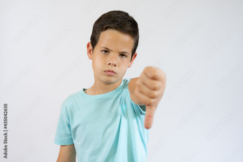 Young little caucasian kid over white background looking unhappy and angry showing rejection and negative with thumb down gesture. Bad expression. Young little caucasian kid over white background looking unhappy and angry showing rejection and negative with thumb down gesture. Bad expression.