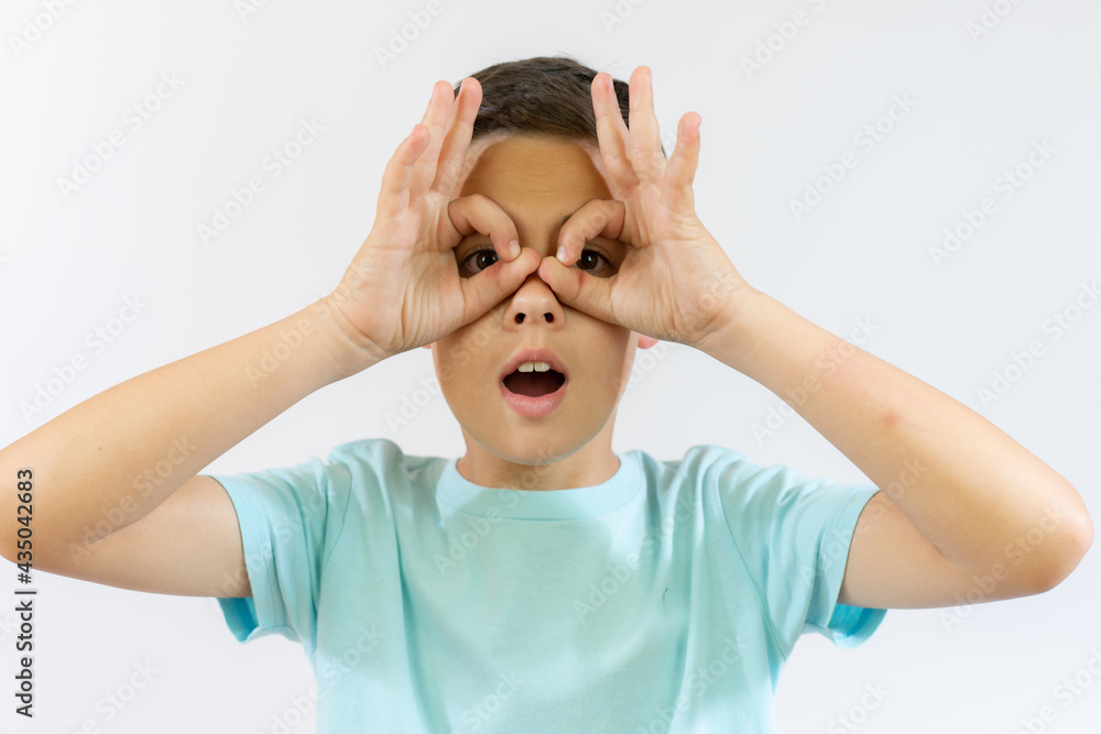 Little caucasian boy kid wearing casual clothes doing okay gesture like binoculars, eyes looking through fingers. crazy expression. Little caucasian boy kid wearing casual clothes doing okay gesture like binoculars, eyes looking through fingers. crazy expression.