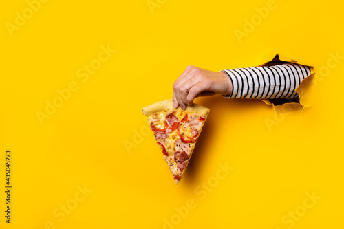 female hand holds a slice of fresh hot pizza on a torn yellow background
