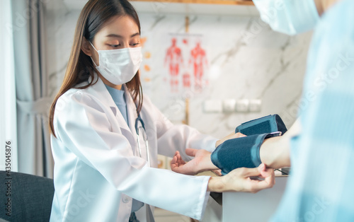 Young woman-doctor is checking her patient's blood pressure, while they are sitting together at the desk in a cabinet. Physician at work in a hospital. Doctor checking blood pressure of the patient,.