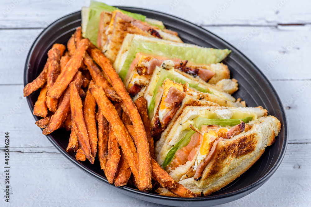 A serving of club sandwiches cut into triangles with sweet potato fries on the side A serving of club sandwiches cut into triangles with sweet potato fries on the side
