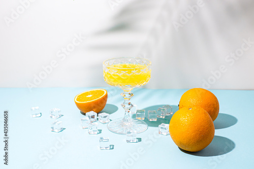 glass with orange cocktail, orange and ice cubes on a blue background