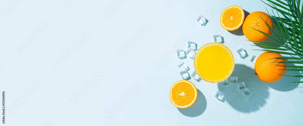 glass with orange juice, orange and ice cubes on a blue background. Top view, flat lay. Banner glass with orange juice, orange and ice cubes on a blue background. Top view, flat lay. Banner
