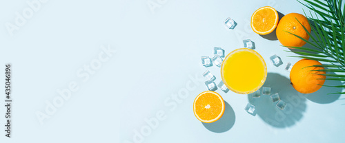 glass with orange juice, orange and ice cubes on a blue background. Top view, flat lay. Banner