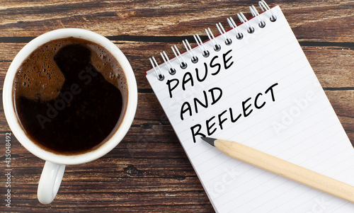 PAUSE AND REFLECT text on notebook with coffee on wooden background photo