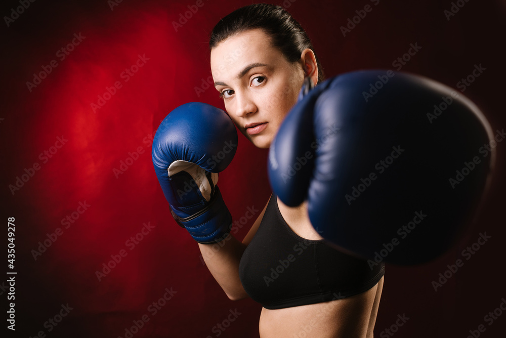 Extreme sport woman boxer wearing blue boxing gloves on dark red background Extreme sport woman boxer wearing blue boxing gloves on dark red background
