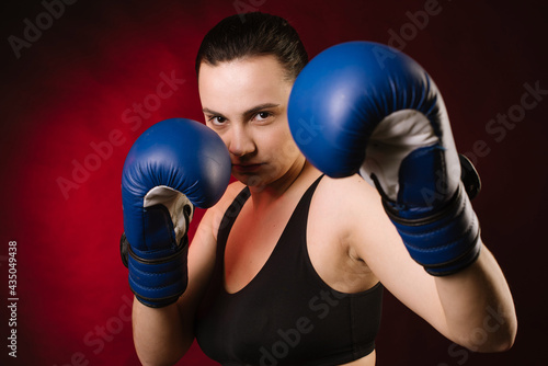 Extreme sport woman boxer wearing blue boxing gloves on dark red background © rostyslav84