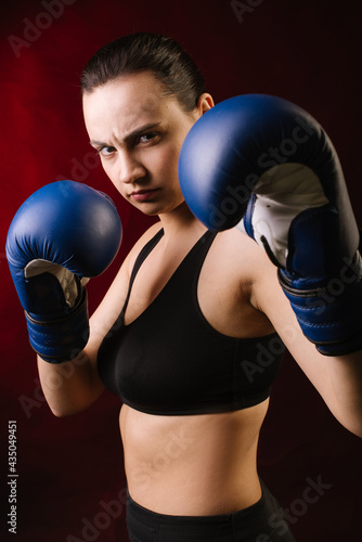 Extreme sport woman boxer wearing blue boxing gloves on dark red background © rostyslav84