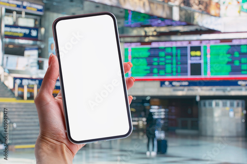 Mockup of a smartphone with a white screen close-up against the background of the timetable at the railway station.
