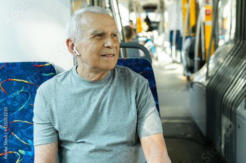 Fototapet Elderly man is using wireless earbuds during ride in public transport