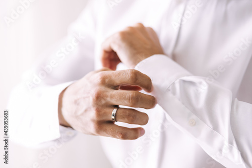 Morning of the groom on the wedding day. Hands of a man straightens his sleeve on a white shirt
