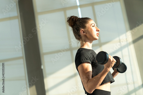 Concept fitness sport training lifestyle. Active sport athletic woman with dumbbells pumping up muscles body.