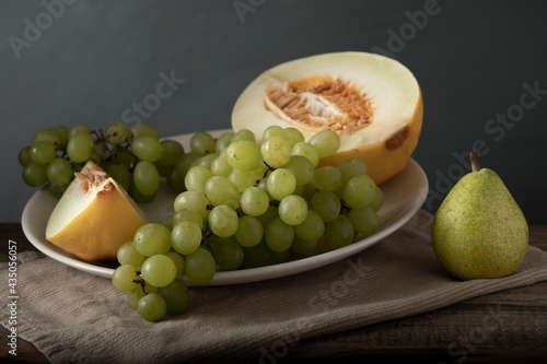 White plate with melon and grape next to pear. Classic still life. Soft light.