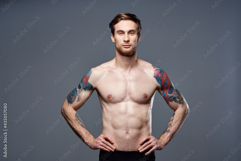 handsome man with a naked pumped-up torso tattoos on his arms holds his hands on his belt