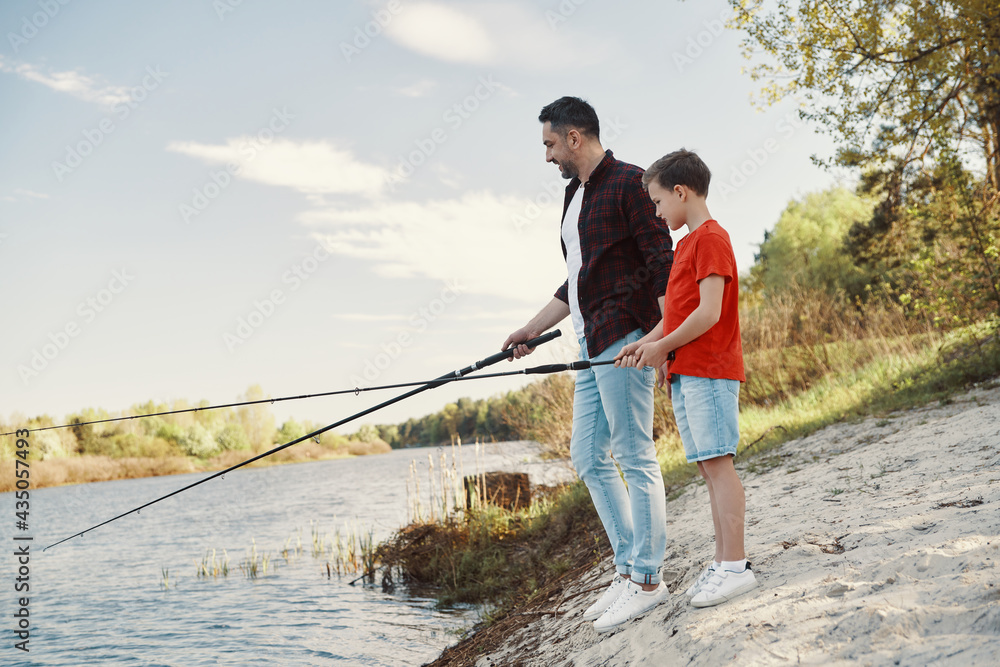 Happy young father teaching his son fishing and smiling while spending weekend together Happy young father teaching his son fishing and smiling while spending weekend together