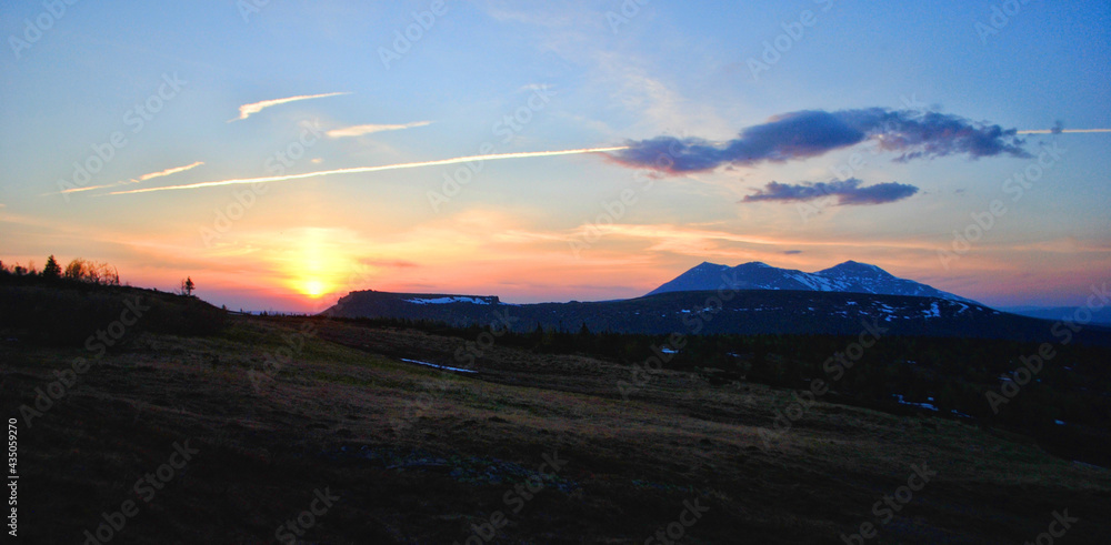 Sunset in the mountainous area against the background of clouds and flying aircraft in the sky