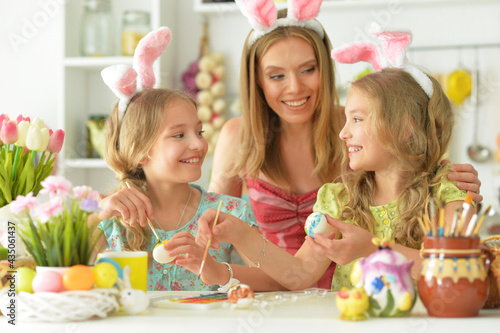  Mother with daughters wearing rabbit ears decorating  Easter eggs