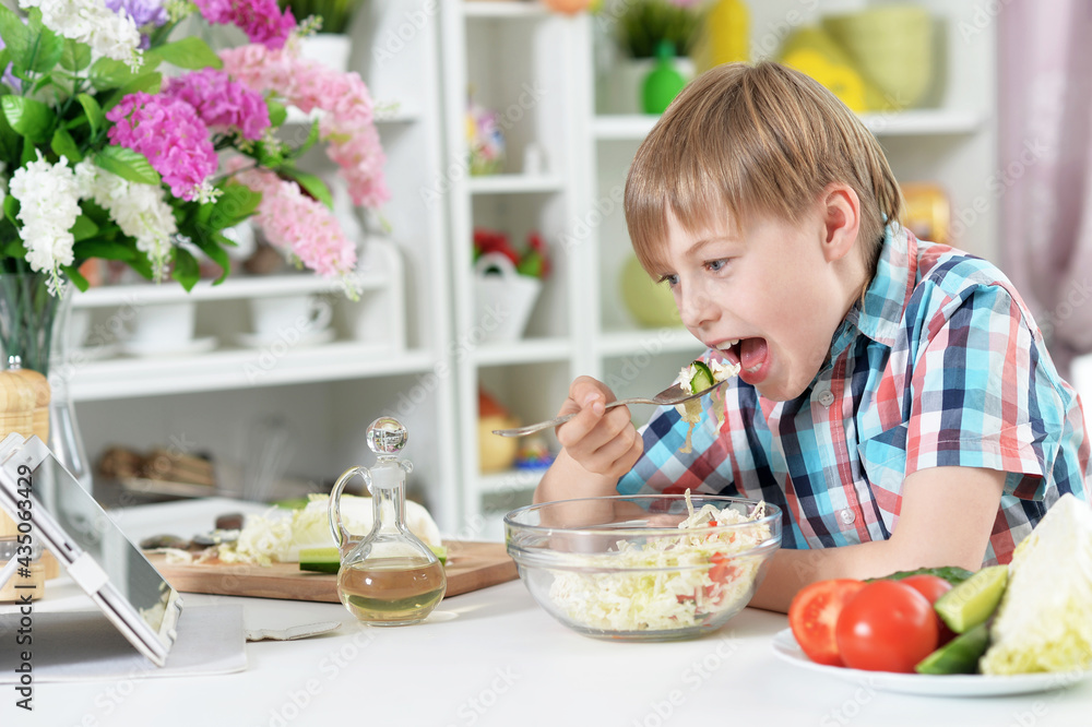 Cute boy eating salad on kitchen table at home Cute boy eating salad on kitchen table at home