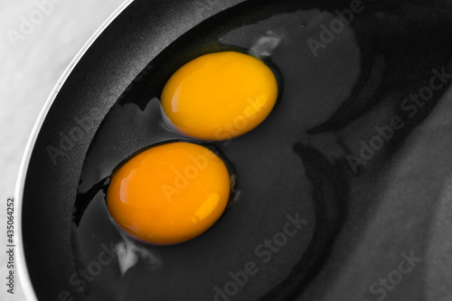 Raw eggs with bright yellow yolks and transparent whites with a clots in a black frying pan. The concept of the process of cooking a simple dish for breakfast. Close-up