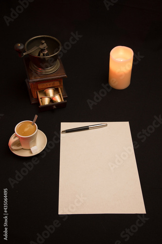 Feuille blanche avec stylo et tasse de café près du moulin à café et éclairé à la bougie et reflet rouge