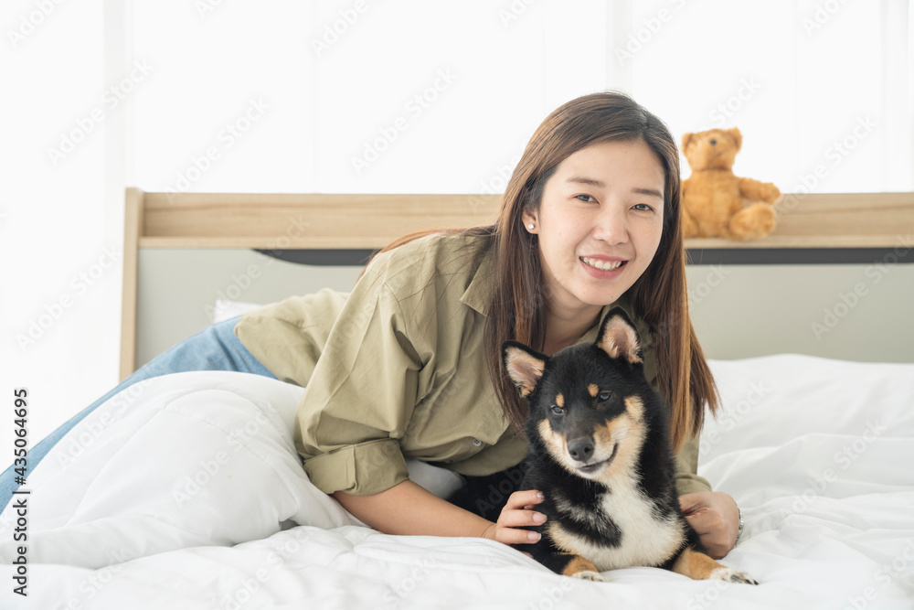 Pet Lover concept. An Asian woman is resting with a Shiba Inu dog on bed in bed room. Shiba Inu is a Japanese dog that is famous throughout the world. Pet Lover concept. An Asian woman is resting with a Shiba Inu dog on bed in bed room. Shiba Inu is a Japanese dog that is famous throughout the world.