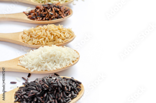 Dry organic white rice seeds in light brown wooden spoon with blur red, brown, and riceberry seeds on white background with copy space