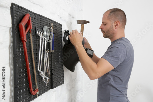 Man organizing his tools on the plastic pegboard on the wall in workshop. photo