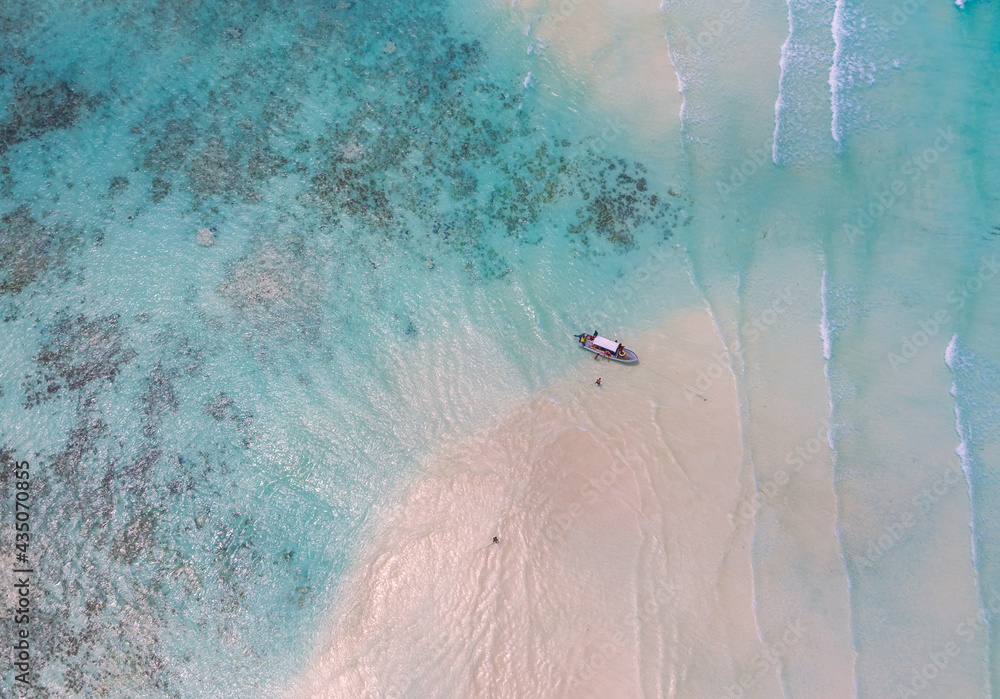 Aerial shot of the Mnemba Island white sand sandbanks washed with turquoise Indian ocean waves near the Zanzibar island, Tanzania. The couple came here on the motorboat, anchored it and having rest.