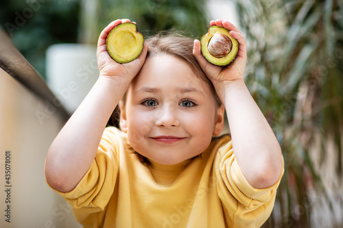 Little girl in yellow sweatshirt holding cut avocado, healthy eating concept