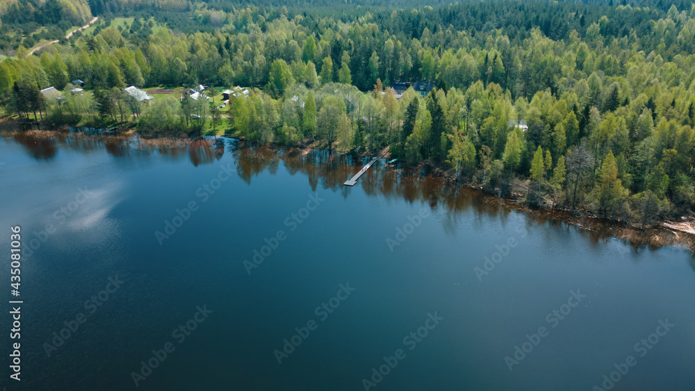 A beautiful scenery, a lake, a forest, a small village from a bird's eye view. Ideal for fishing, pontoon bridge. The clouds are reflected in deep water. Aerial photography, view from a drone.