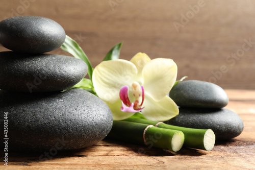 Spa stones, bamboo stems and beautiful orchid flower on wooden table, closeup