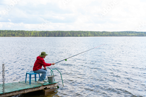 Fotobehang A fisherman with a hat with a fishing rod sits on the bank of the river