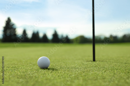 Golf ball near hole on green course, space for text
