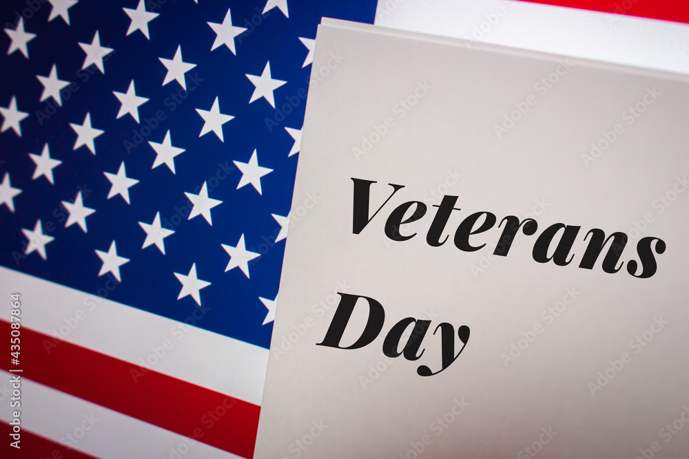 Conceptual keyword Veterans Day, a federal holiday in US observed annually on Nov 11 for honoring military veterans, on card on US flag from a little bit diagonal angle.