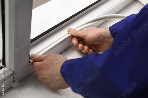 Worker putting rubber draught strip onto window indoors, closeup