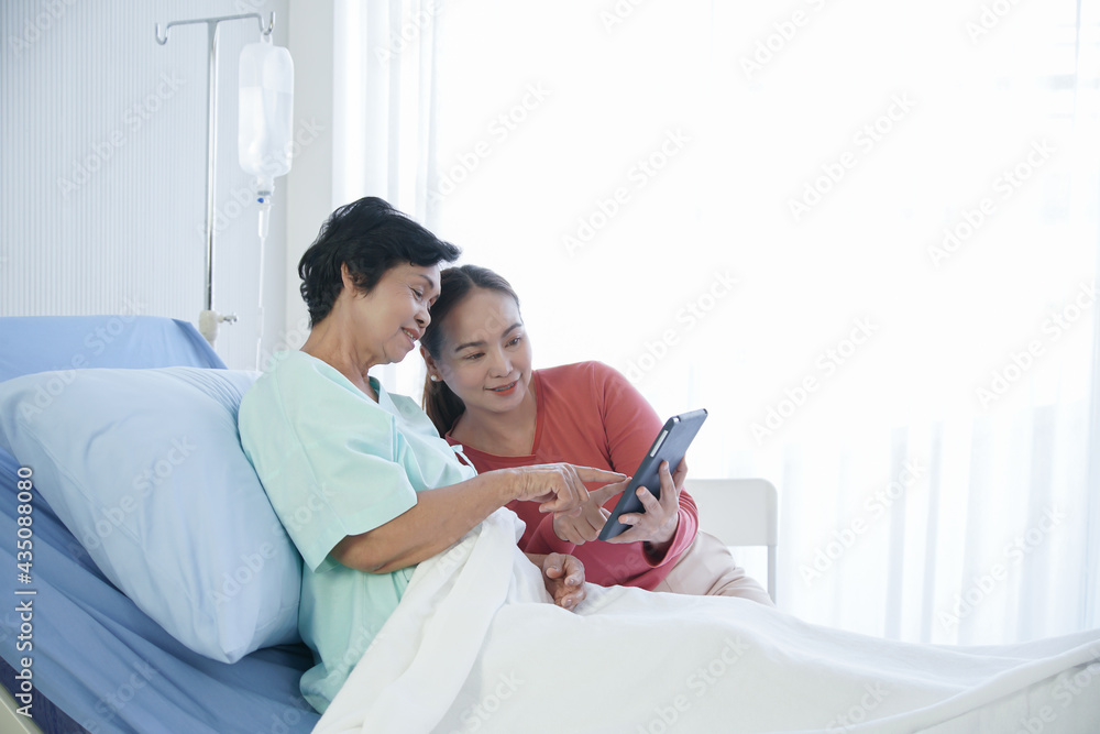 Asian young daughter caring of senior mother patient. They enjoy using tablet together after mom get treatment at hospital