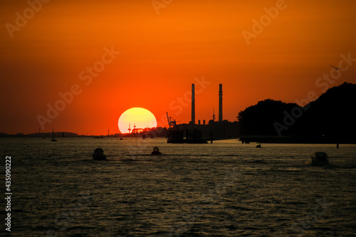 große untergehende Sonne mit tief orangem Himmel und Industriekulisse im Vordergrund