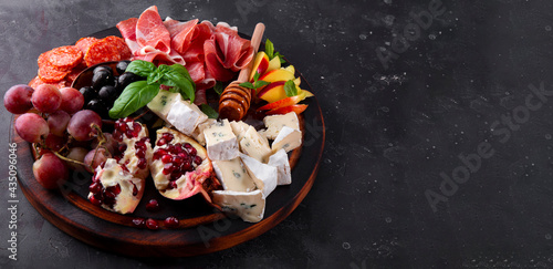 Banner for website. A set of appetizers for wine, jamon, pepperoni, cheese, grapes, peach and olives on a wooden board. Snack board on dark gray background, free space for text