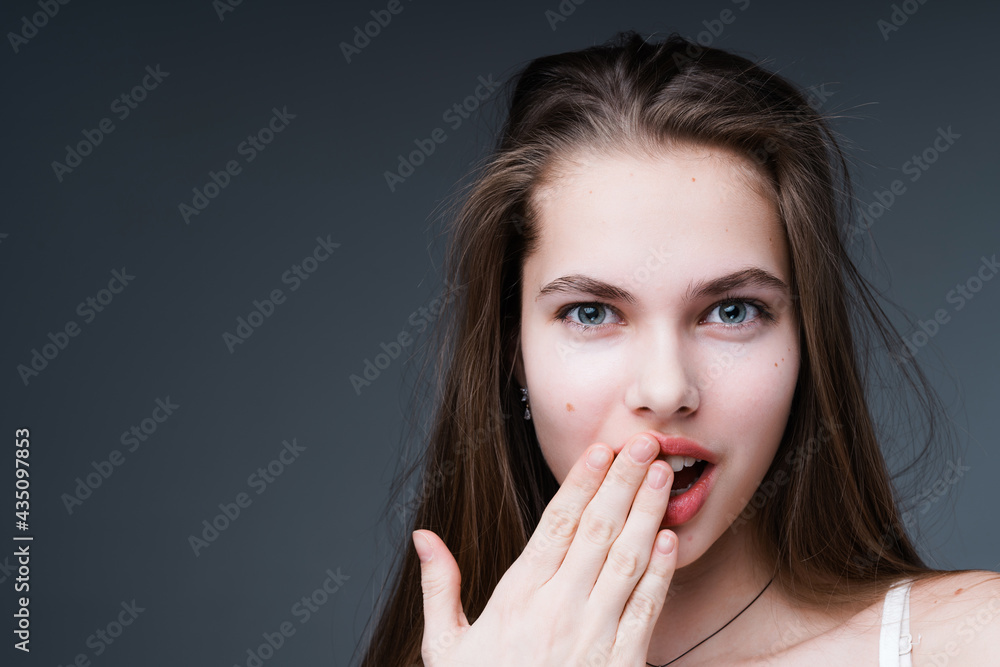 Attractive girl is surprised looking into the camera and applying a hand to her mouth. Isolated on dark background Attractive girl is surprised looking into the camera and applying a hand to her mouth. Isolated on dark background
