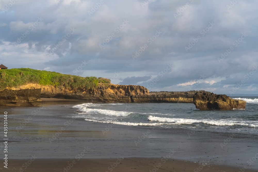 Beautiful volcanic black sand beach with big rocks and cliffs on shore