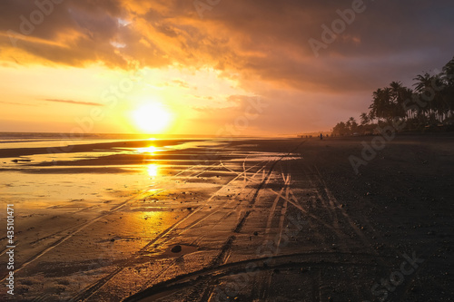 Empty black sand beach with bike trails during beautiful orange sunset