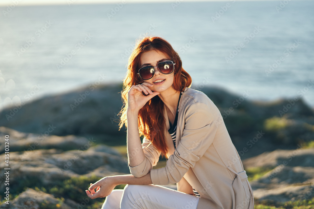 woman in a jacket and t-shirt in the mountains near the sea on the beach and glasses on her face