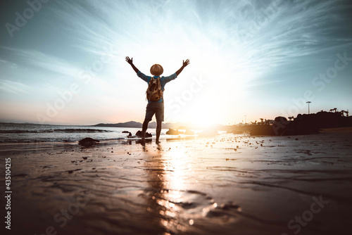 Man with arms up on the beach at sunset - Happiness and wellbeing concept