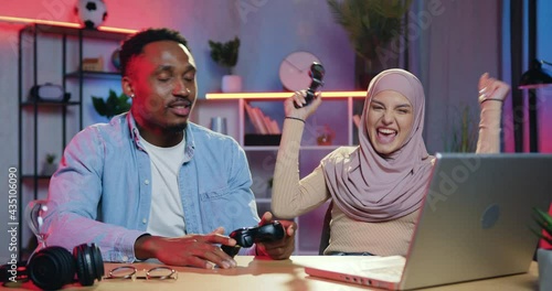 Human emotions concept where attractive positive modern young mixed races female and male friends having fun together at gaming on laptop,woman winning and deriding over mate-loser photo