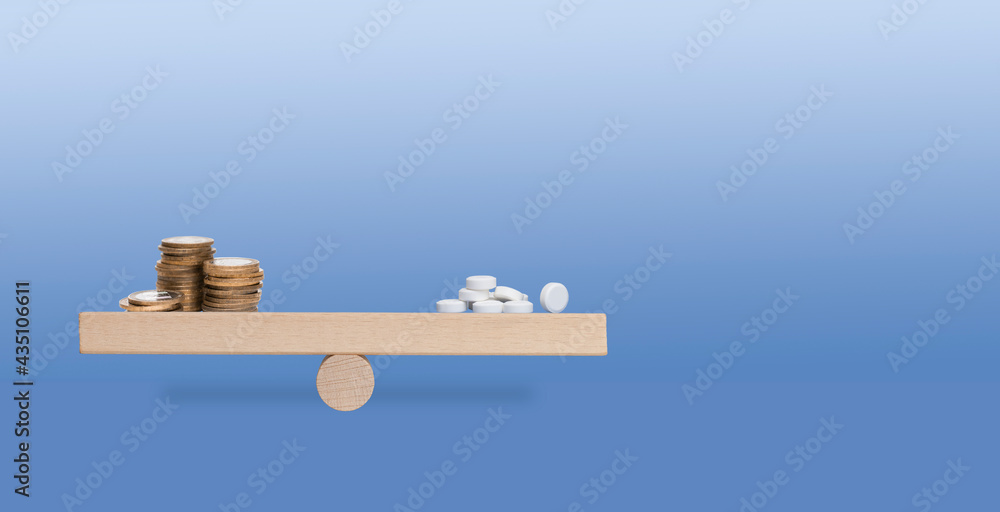wood scales with golden stack of coins and white pills on the blue background with copy space wood scales with golden stack of coins and white pills on the blue background with copy space