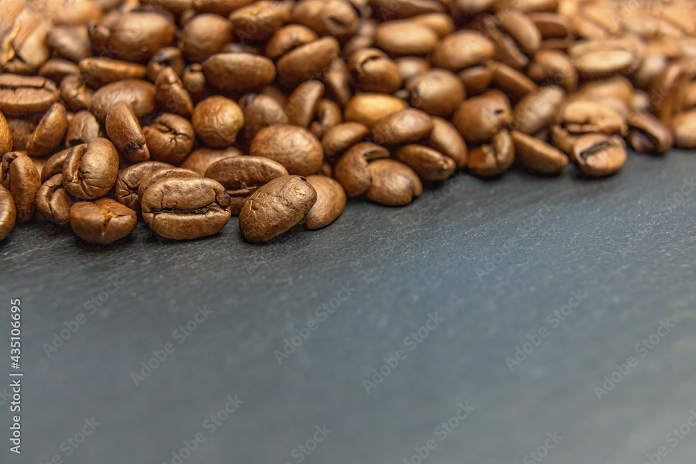 Heap of coffee beans lying on a dark slate desk forming the top edge of a photo. Heap of coffee beans lying on a dark slate desk forming the top edge of a photo.