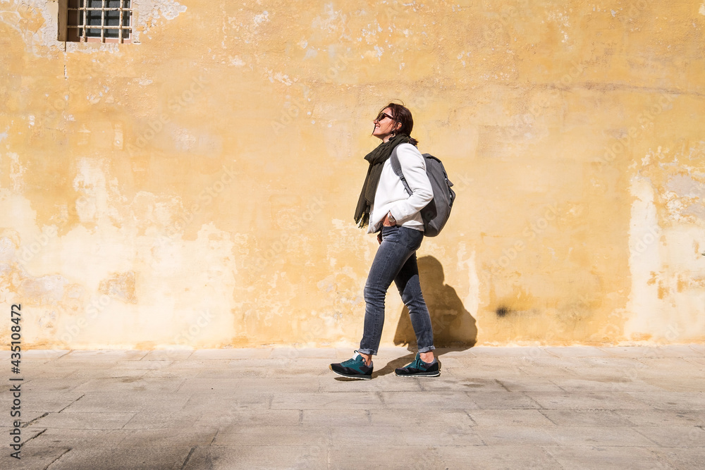Tourist walking by the ancient medieval Mdina streets with a city backpack and enjoying a historical place. Smiling Female traveling alone on the Malta island. Tourist walking by the ancient medieval Mdina streets with a city backpack and enjoying a historical place. Smiling Female traveling alone on the Malta island.