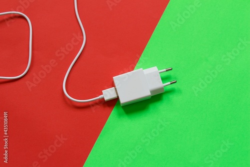 White phone charger isolated on half red half green background. Technological devices. Top view.