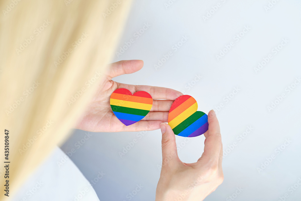 Fototapeta premium Rainbow heart from paper in woman hands in white t-shirt. LGBT flag. LGBTQIA Pride Month in June. Lesbian Gay Bisexual Transgender. Gender equality. Human rights and tolerance. Rainbow flag
